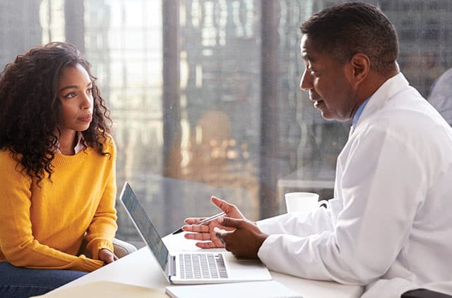 A male doctor sitting across from a woman having a discussion with a laptop