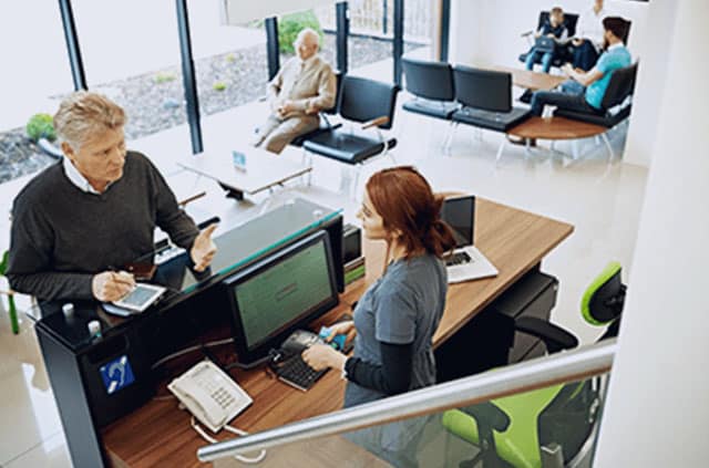 Healthcare worker at front desk talking to a patient while they pay for their healthcare services
