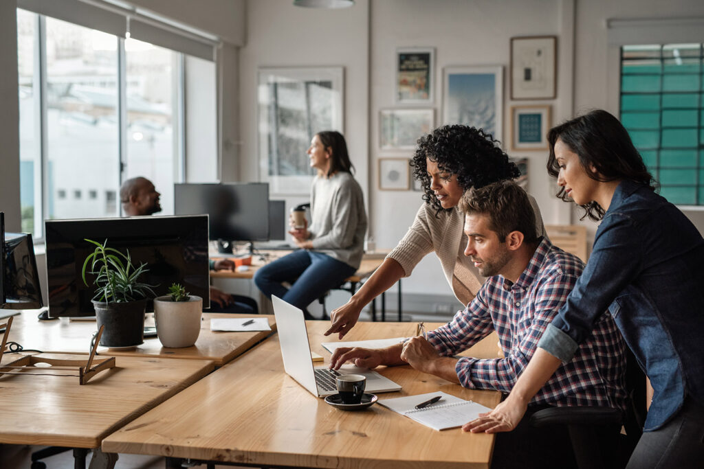 an image of coworkers gathered around a laptop in discussion